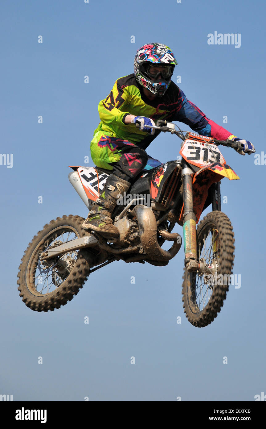 Motocross is a form of motorcycle racing held on rough enclosed off-road circuits. Motorbike rider on scramble bike, jumping high in blue sky Stock Photo