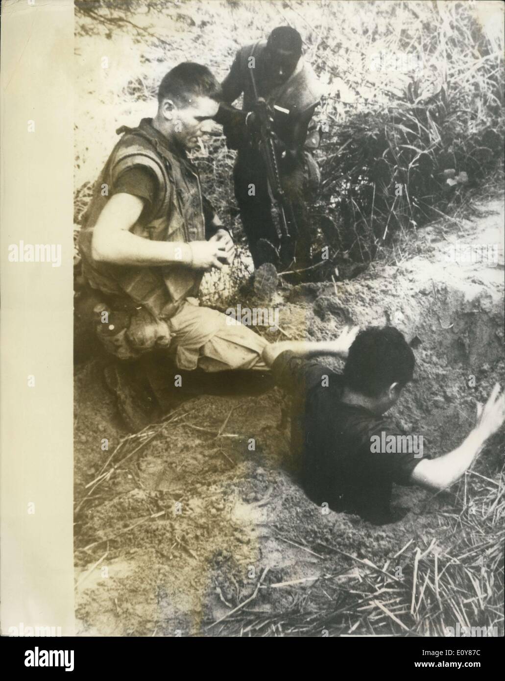 Jan. 14, 1969 - Flushing A ''Fox''. A Viet Cong sniper is flushed from his hole by two U.S. Marines 22 miles south of Da Nang. The Marine calmly smoking a cigarette has his hands around a grenade ready to pull the pin if the prisoner has any pals in the underground bunker who will not come out, while another Marine covers the man with his automatic rifle. Stock Photo