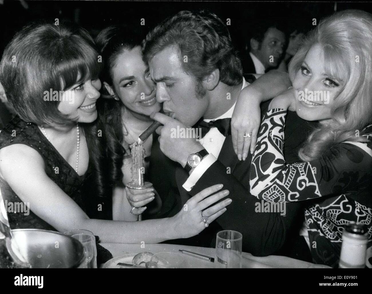 Feb. 03, 1969 - Like a rooster in a cage, the ''unlucky devil'' from Mexico, Olympic participant and actor Uwe Beyer is surrounded by charming film and television actresses, in the Mainz Rheingold hall. Kai Fischer, Karin Dor, and Maria Brockerhoff(from left to right) insist on lighting the cigar to symbolically ''encourage'' the film and athletic heroes. Stock Photo