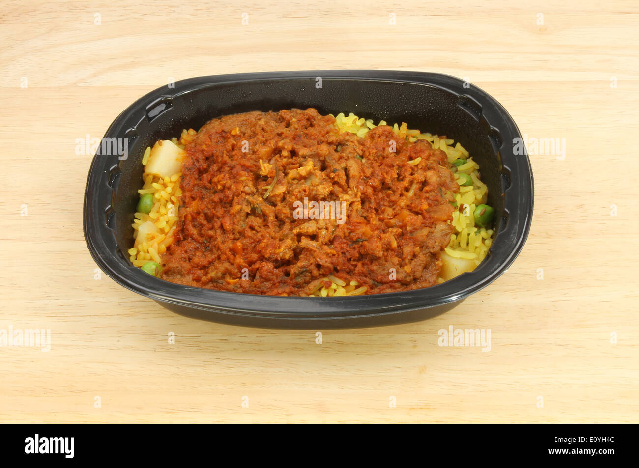 Convenience meal, lamb biryani, in a plastic tray on a wooden tabletop Stock Photo