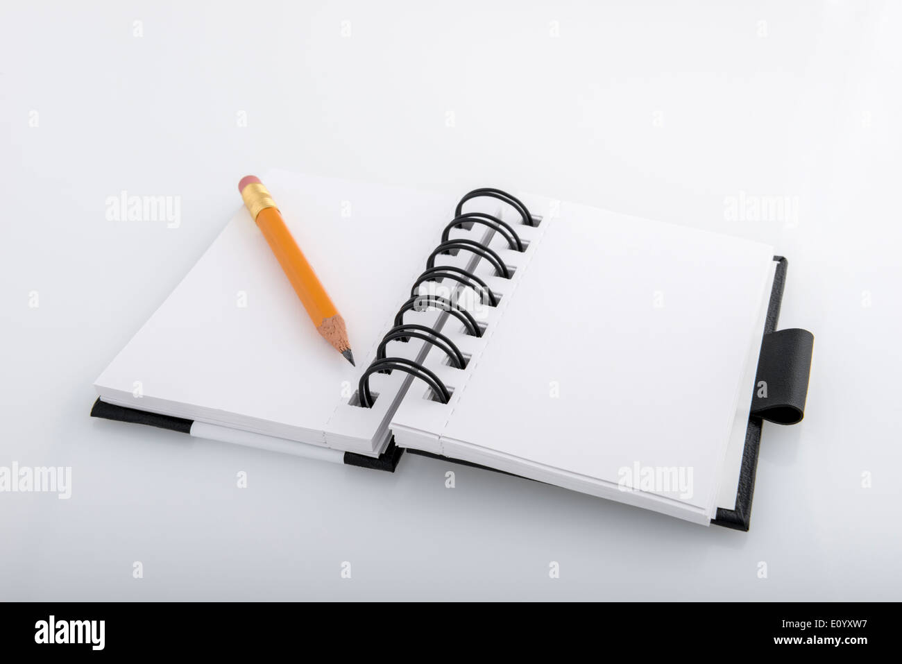 Open black and white ringed notepad and pencil resting on a white desk Stock Photo
