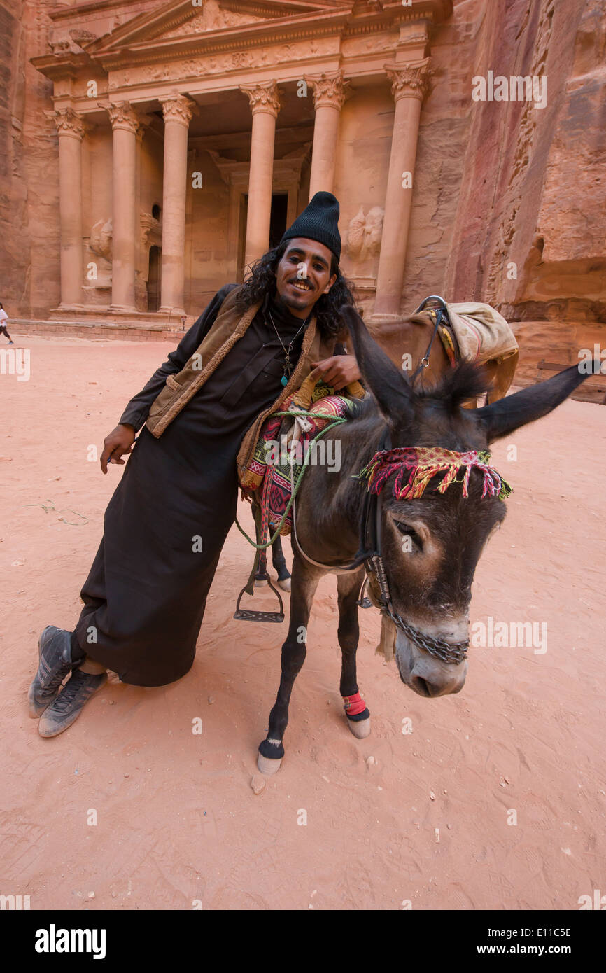 Young Bedoiun man in in a black robe, leaning on his donkey in front of Al Khazneh, (the Treasury), Petra, Jordan Stock Photo