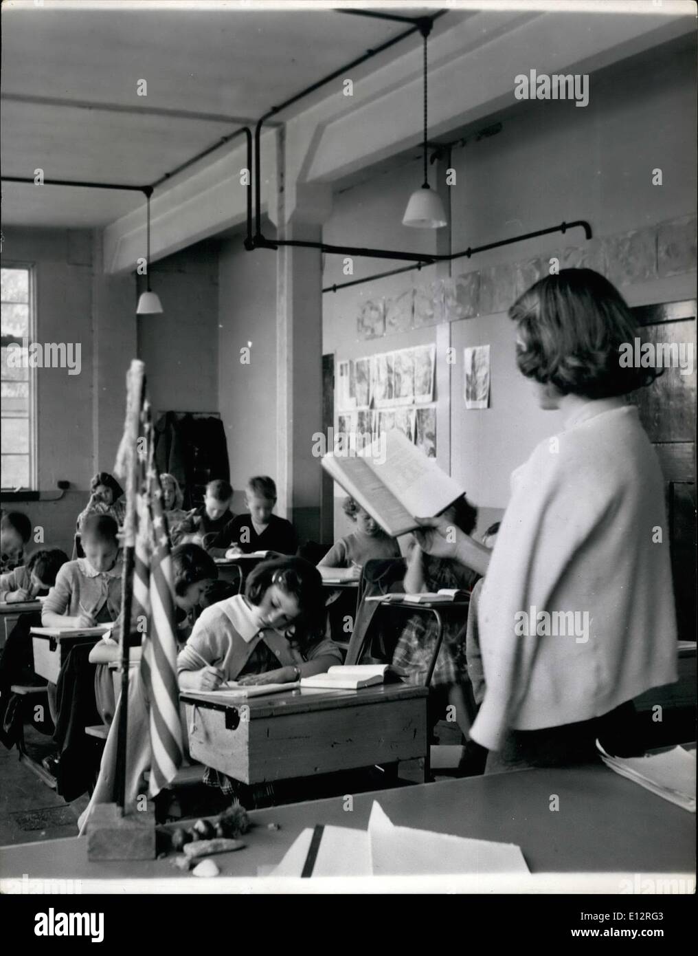 Feb. 25, 2012 - Teacher Miss Constance Colthurst of Charlottesville, Virginia, reads to her pupils in the 4th Grade. School follows the American Customs of having the stars and Stripes on a pedestal on the desk.American Co-ed School Opens Bushey Park: Just near Hampton Court Palace when Henry VIII strolled, the boys and girls of the New World are going to school, They are children of United States Military Personnel stationed in and around London and the School is situated in Bushey Park. There us a Central High School for 210 children and an elementary school for the first eight grades Stock Photo