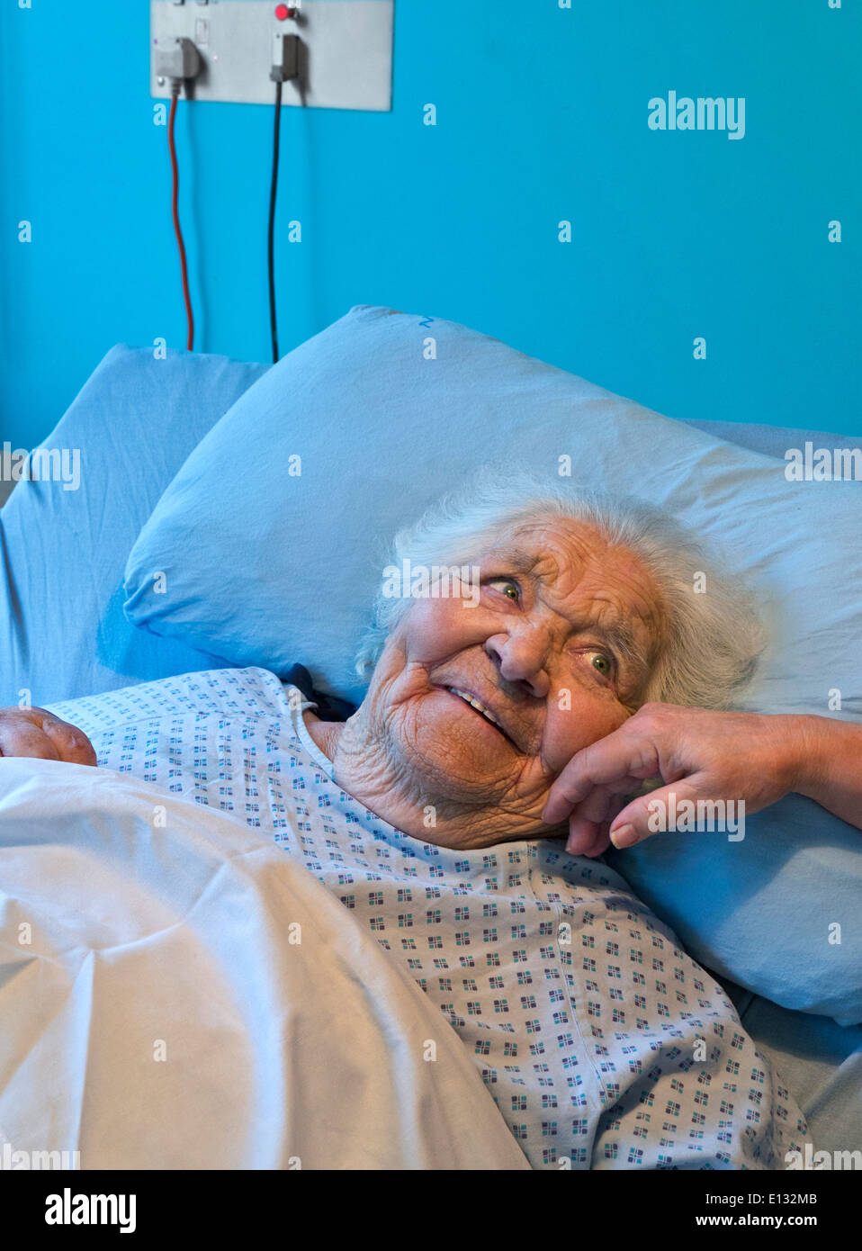 ELDERLY LADY CARE BED SMILING TOUCHING Contented smiling senior old age alert elderly lady secure in care bed with comforting hand of carer nurse Stock Photo