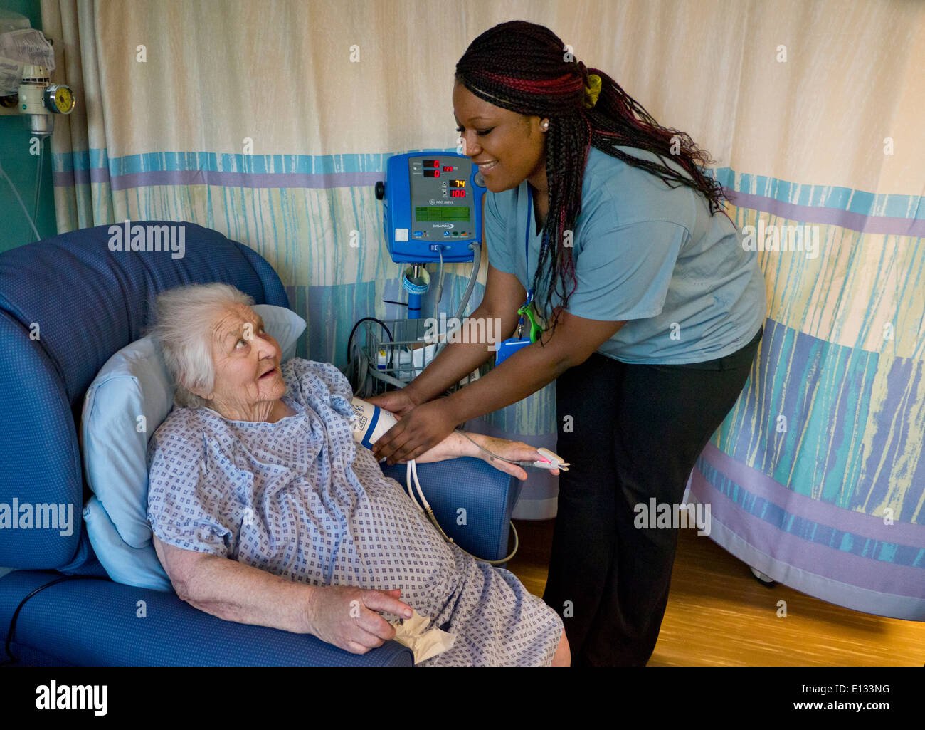 Nurse and elderly senior lady in NHS hospital ward having her blood pressure taken Attractive smiling caring hospital nurse Stock Photo