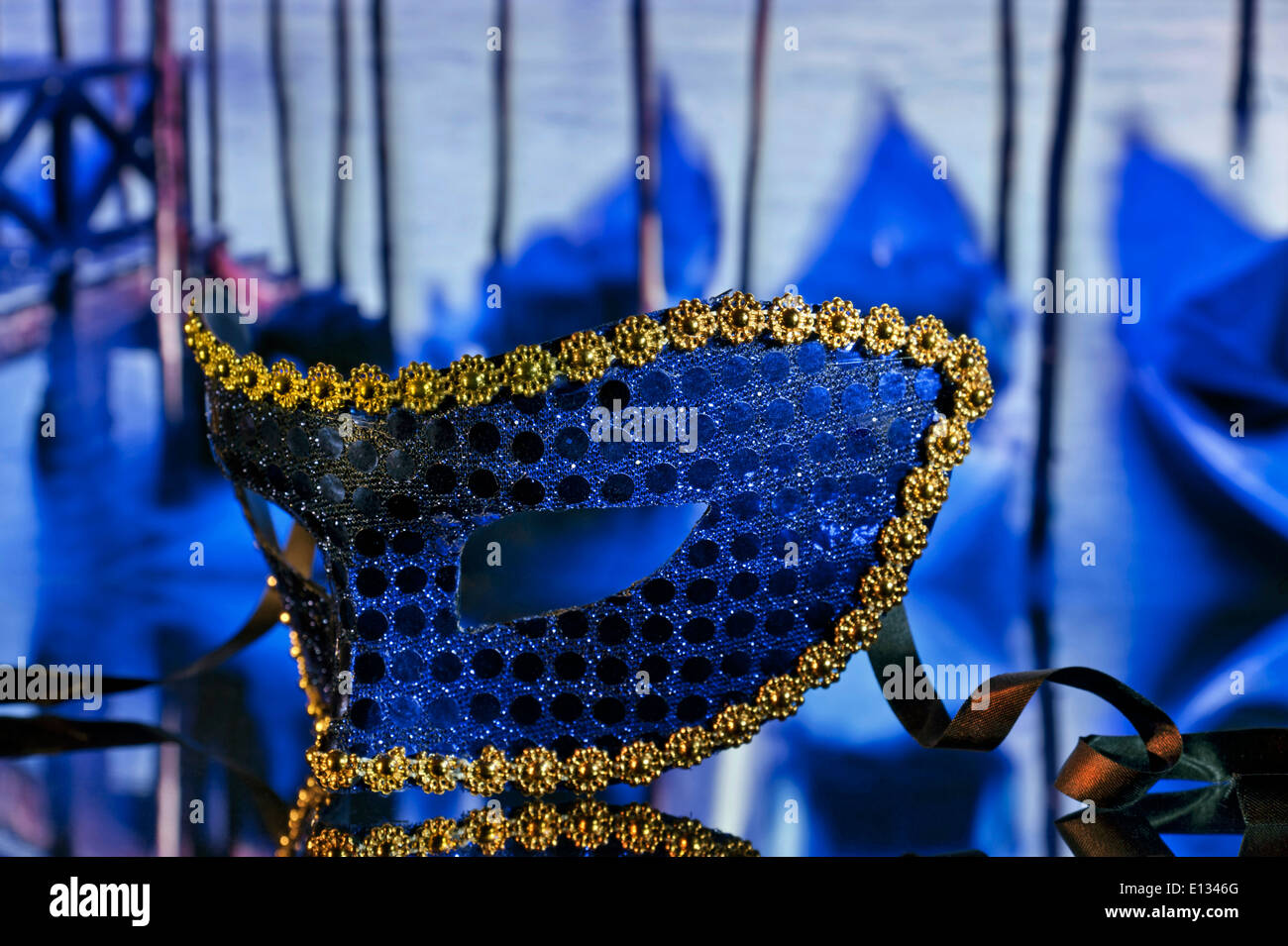 Atmospheric mysterious traditional Venetian carnival mask on cafe table with gondolas behind St Marks Square Venice Italy Stock Photo