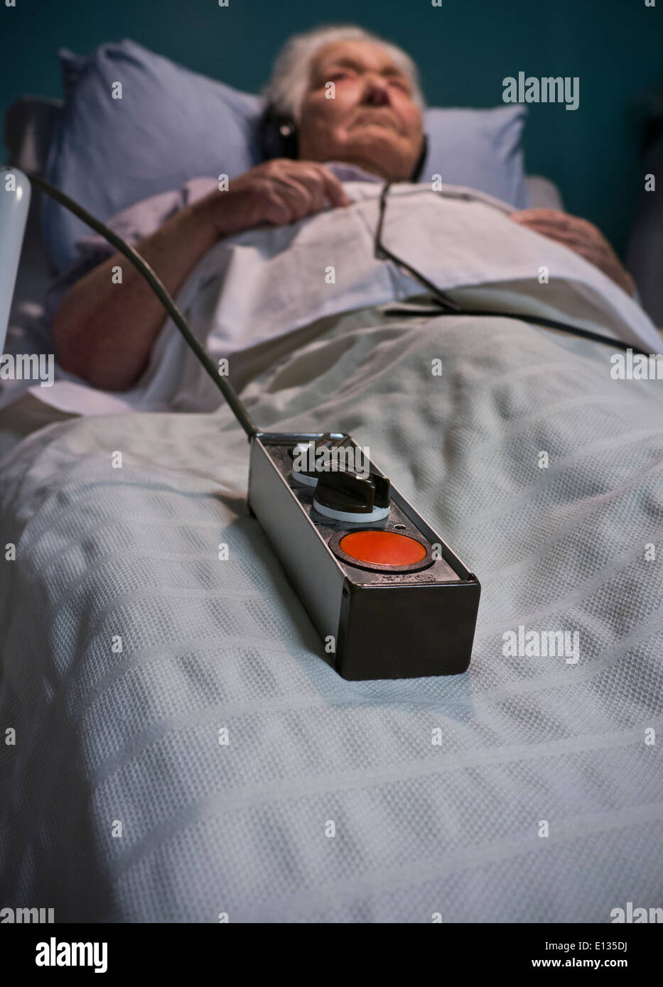 EMERGENCY CALL BUTTON CARE Elderly lady wearing headphones in hospital care bed at night with emergency call button lying to her side Stock Photo