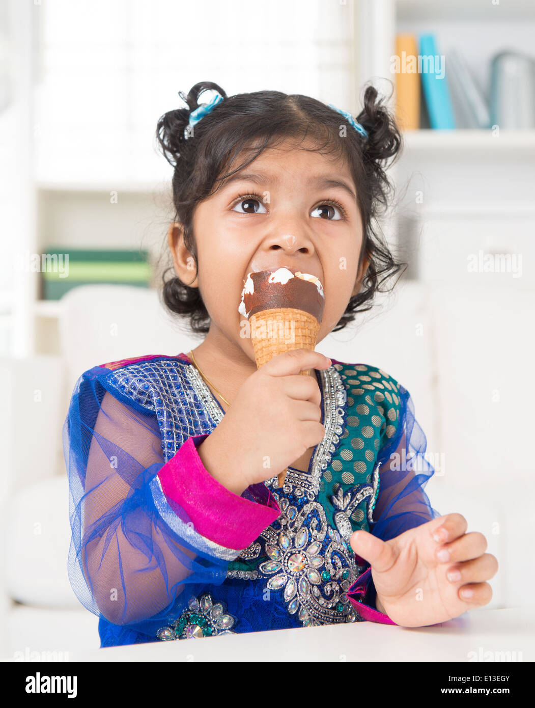 Eating ice cream. Cute Indian Asian girl enjoying an ice cream. Beautiful child model at home. Stock Photo