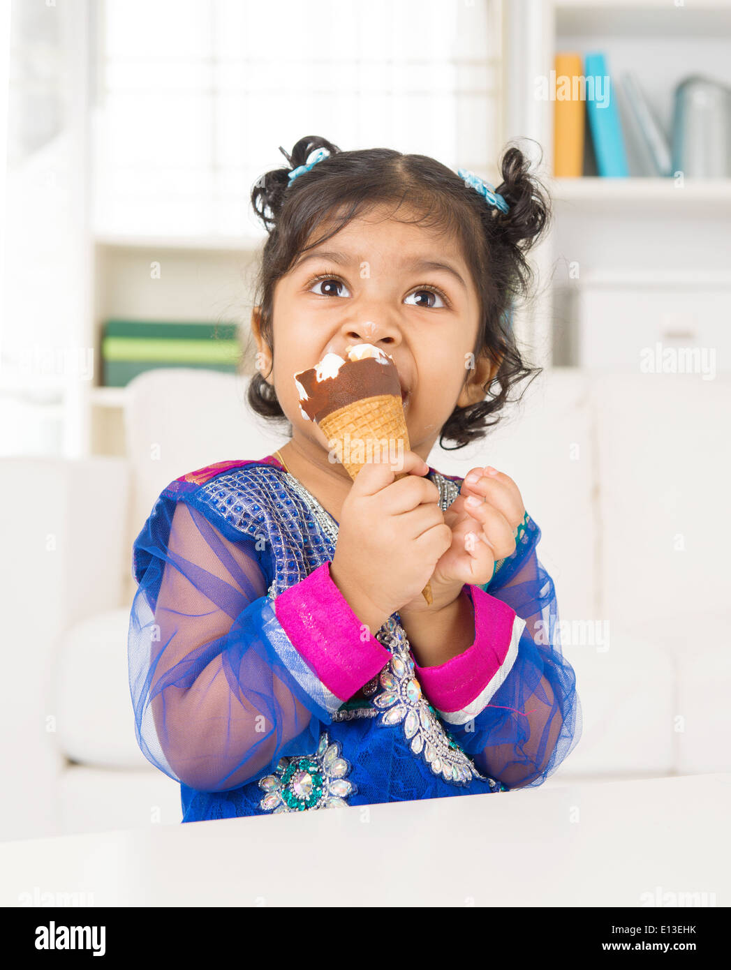 Eating ice cream. Indian Asian girl enjoying an ice cream. Beautiful child model at home. Stock Photo