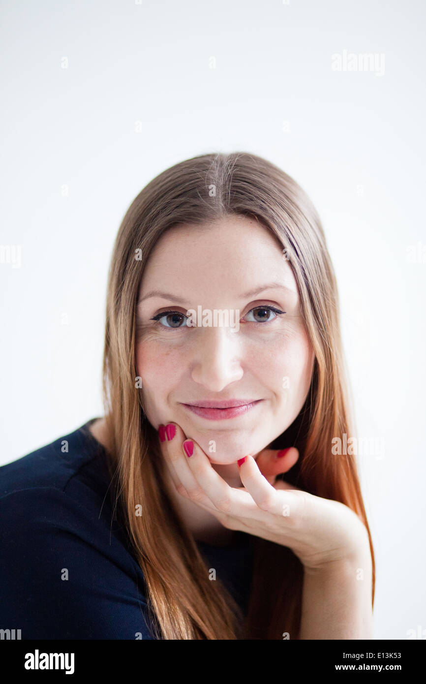Closeup studio portrait of face of happy smiling attractive woman wearing blue blouse and resting chin on hand Stock Photo