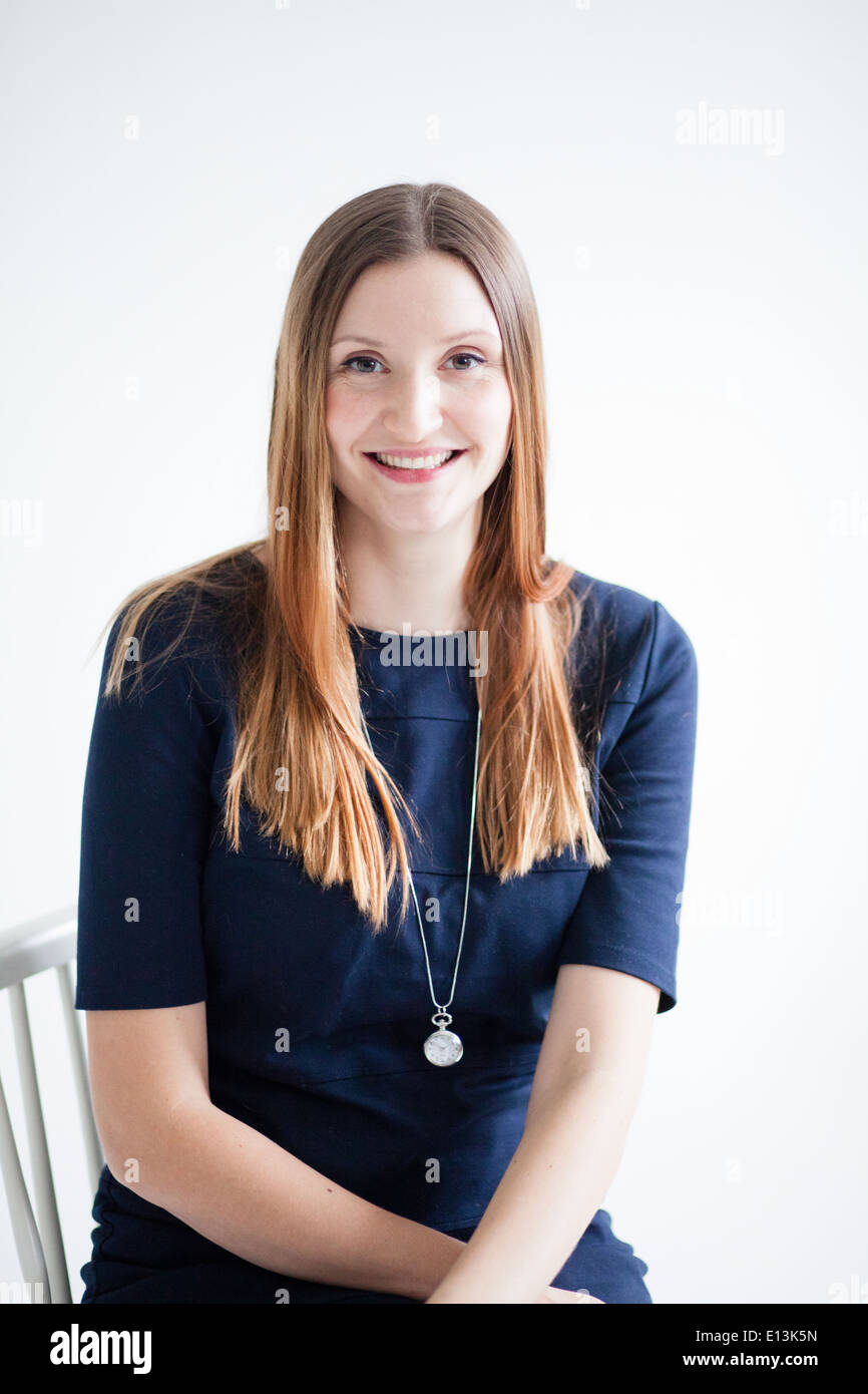 Studio portrait of happy smiling attractive woman wearing blue blouse and sitting in chair with arms crossed Stock Photo