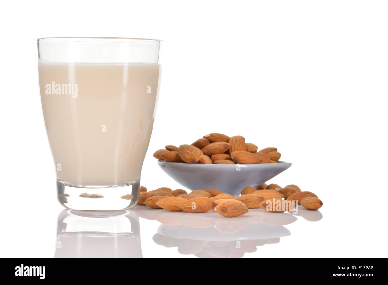 Almond milk as a substitute for dairy milk. Glass of almond milk and few almonds on a saucer isolated on white background. Stock Photo