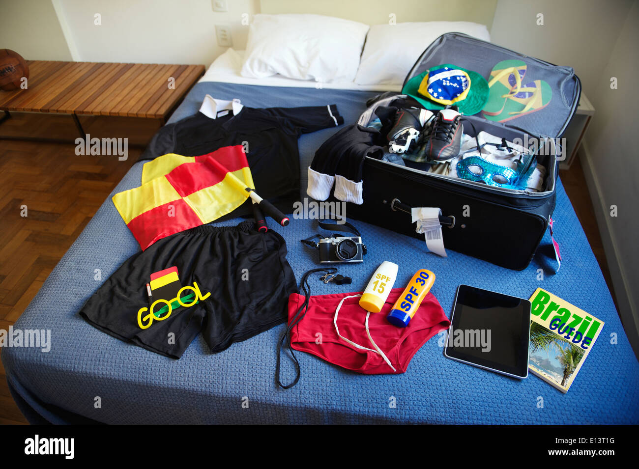 Suitcase packed for football referee trip to Brazil including red and yellow flags, whistle, camera, sunscreen, and guidebook Stock Photo