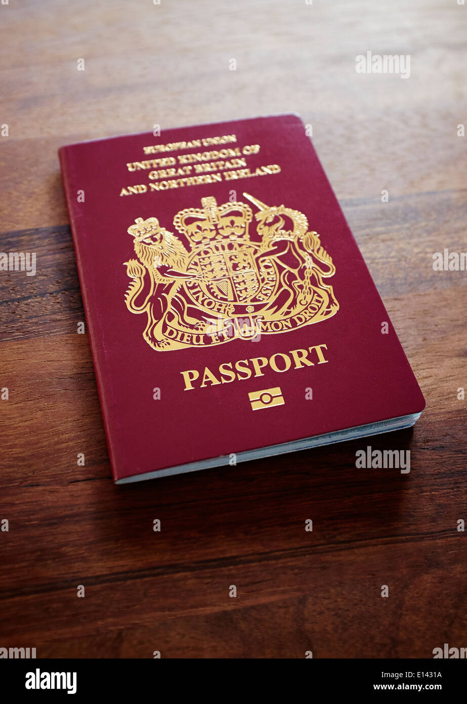 An old EU style pre Brexit burgundy UK Passport on a dark wood table top background. Stock Photo