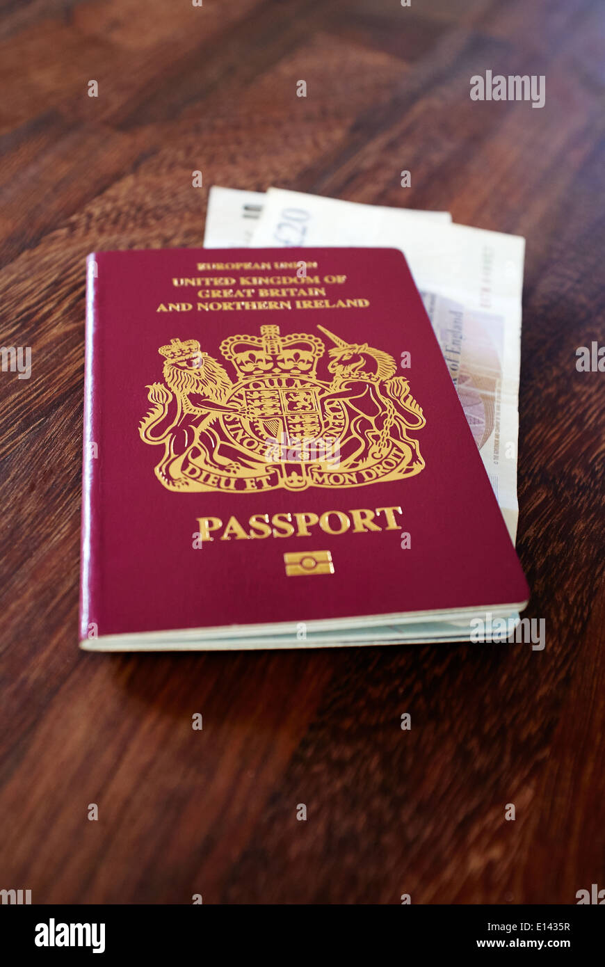 An old EU style pre Brexit burgundy UK Passport with old GBP Sterling bank notes on a dark wood table top. Stock Photo