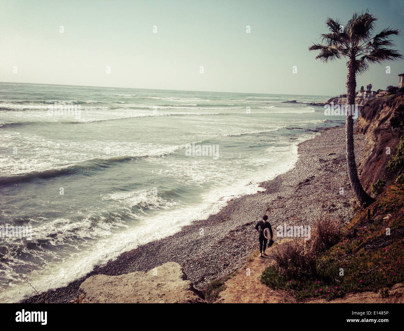 Surfer walking on rocky beach, San Diego, California, United States - Smartphone Captured Stock Image