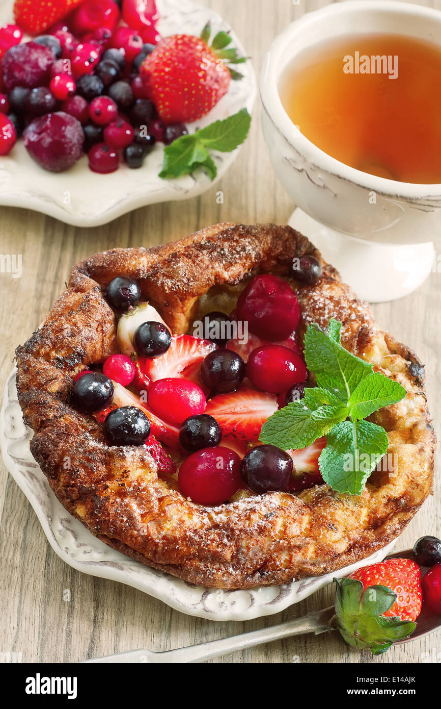 Mini german pancake with mix of berries and tea. Selective focus. Stock Photo