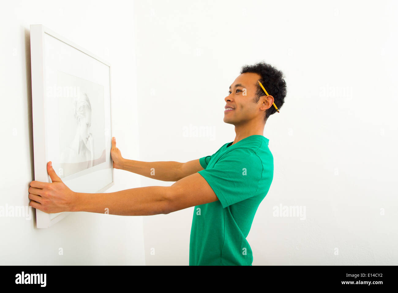 Mixed race man hanging picture on wall Stock Photo