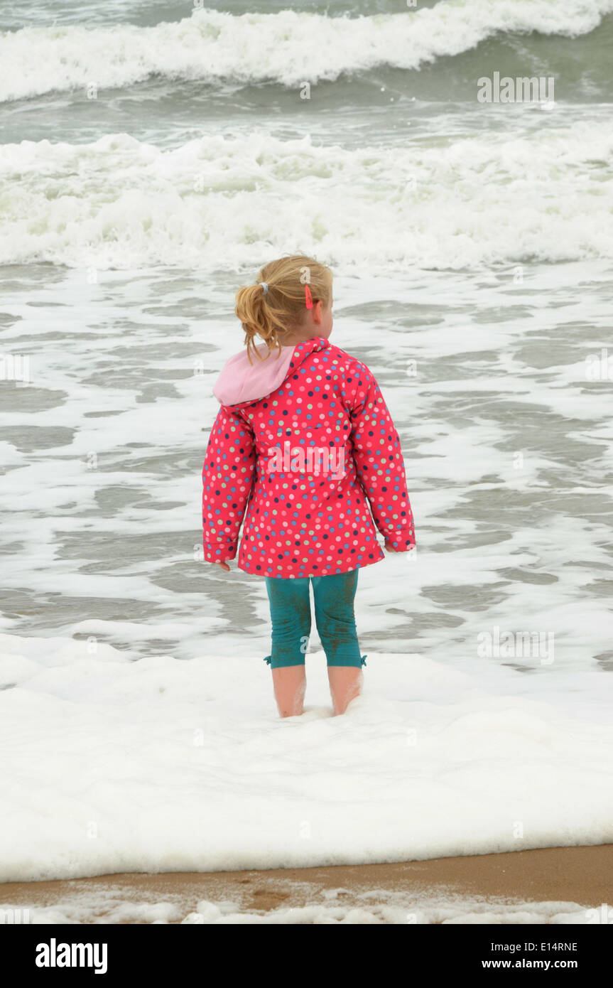 a young girl standing in rough seas on a chilly summer day. Stock Photo
