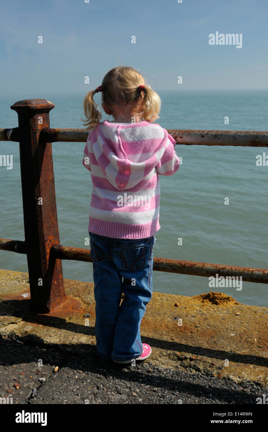 young girl standing by rusty railings at the beach Stock Photo