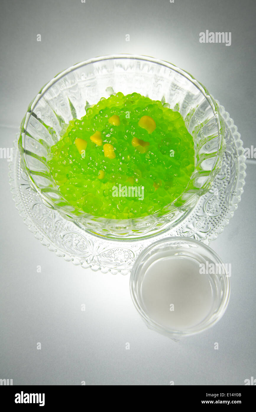 Thai Sago Sagu Pudding green pearls with corn yellow seeds [served warm] coconut milk tumbler crystal glass saucer Stock Photo