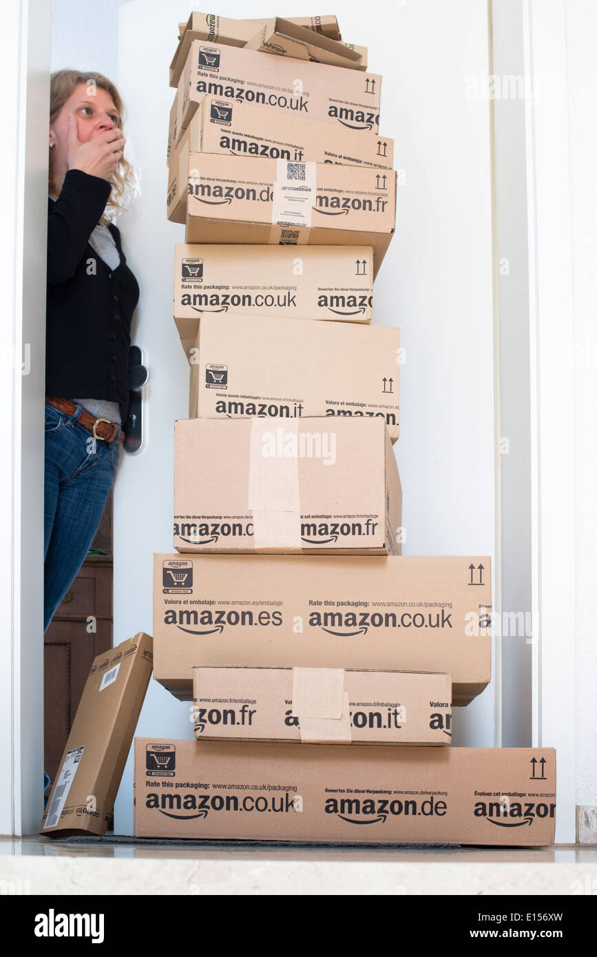 A woman is horrified by a large stack of parcels by Amazon.com in different sizes waiting in front of the entrance door to her f Stock Photo