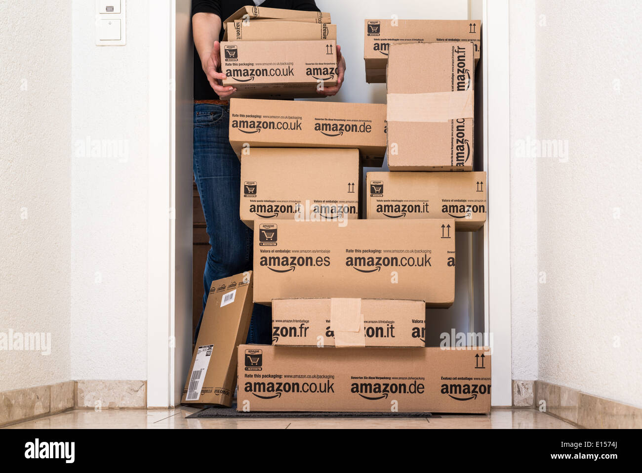A woman is horrified by a large stack of parcels by Amazon.com in different sizes waiting in front of the entrance door to her Stock Photo