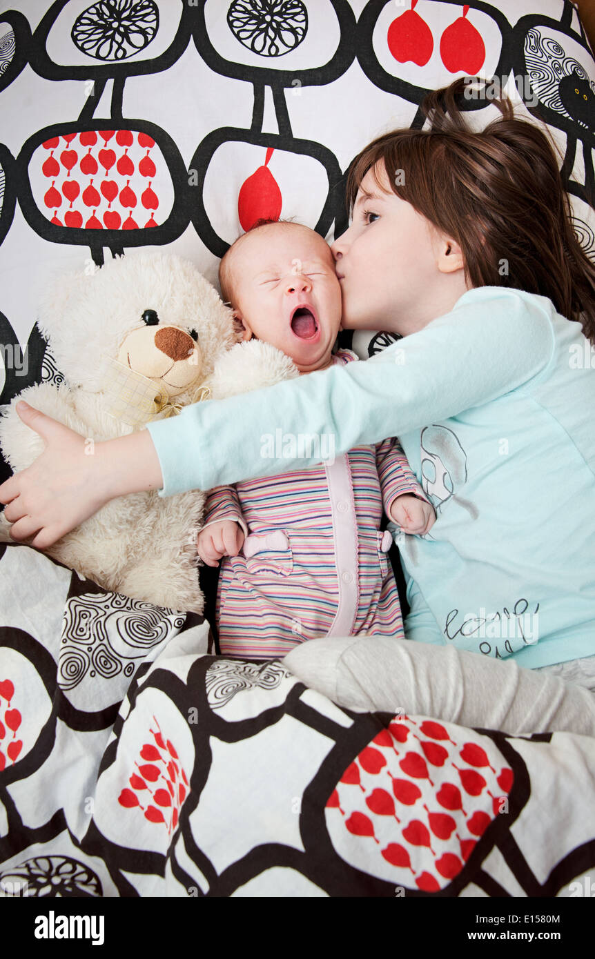 Portrait of little girl kissing her newborn sister with teddy bear Stock Photo