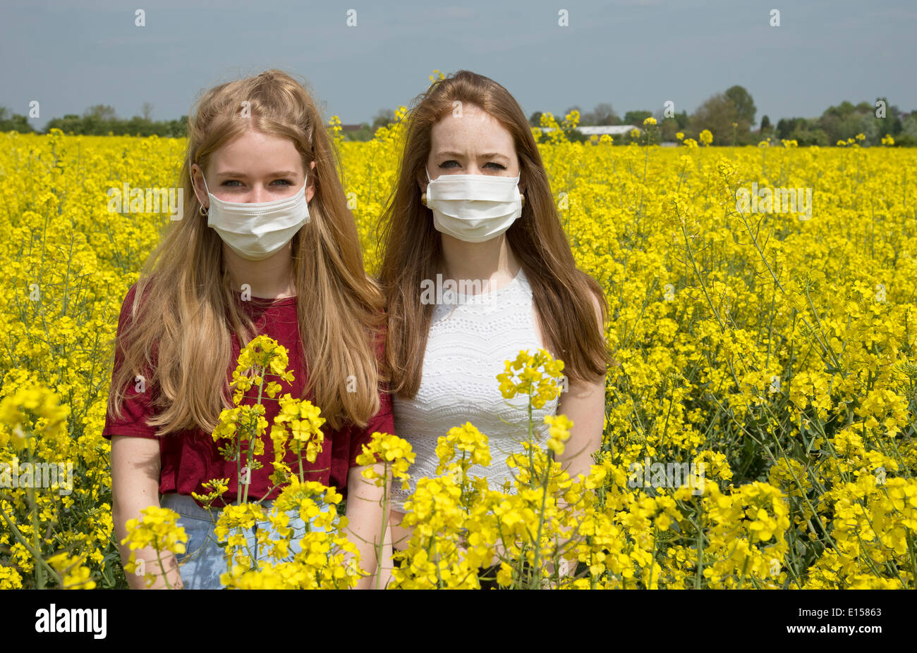 Portrait of two teenage girls in a field of rapeseed wearing a face ...