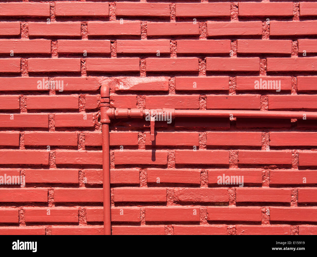 Red brick wall with water pipes and shut-off valve open. Stock Photo