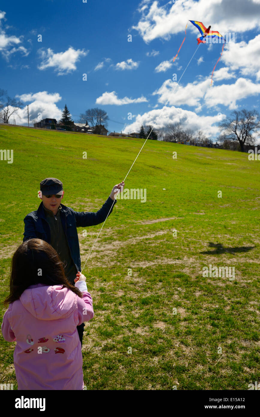 Father teaching young daughter to fly a kite in spring at Riverdale Park Toronto Stock Photo