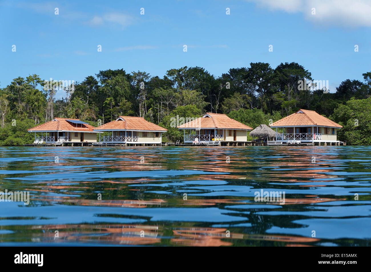 Vacation houses over the sea with ripples of water surface and tropical vegetation in background Stock Photo