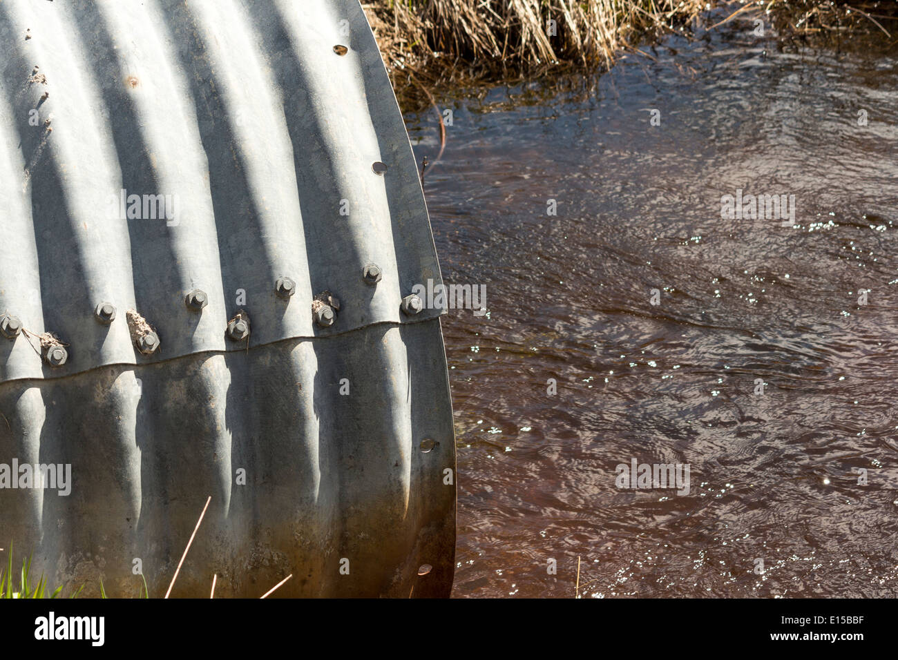 Water from a creek flows out a sewer pipe that runs under a road Stock