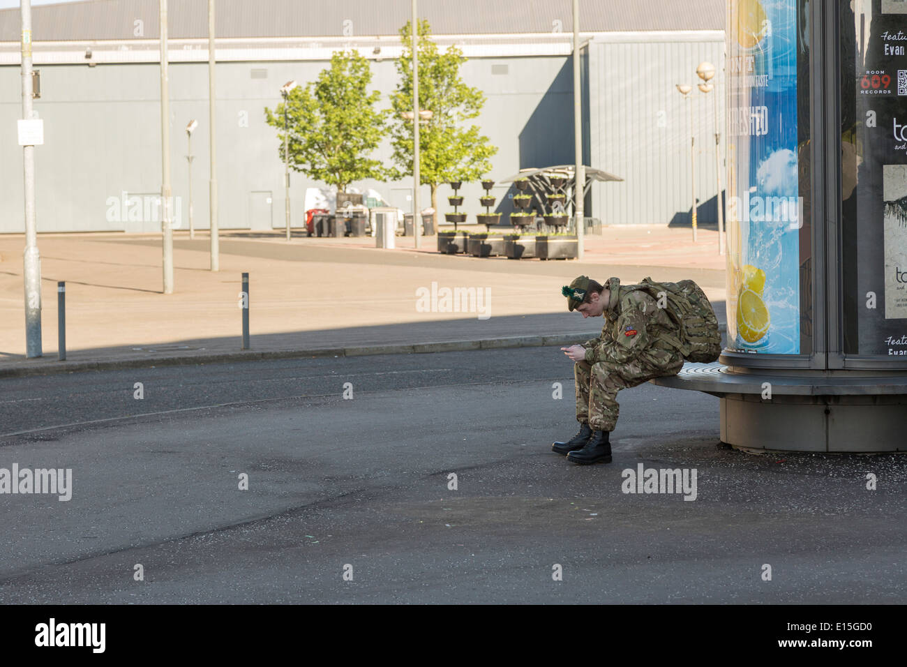 Young male army soldier sits in uniform playing on his smartphone, Glasgow, Scotland, UK Stock Photo