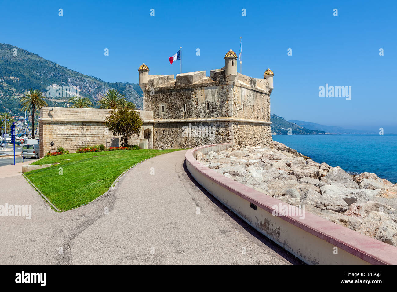 Promenade along Mediterranean sea coastline and small medieval fortress under blue sky in Menton, France. Stock Photo