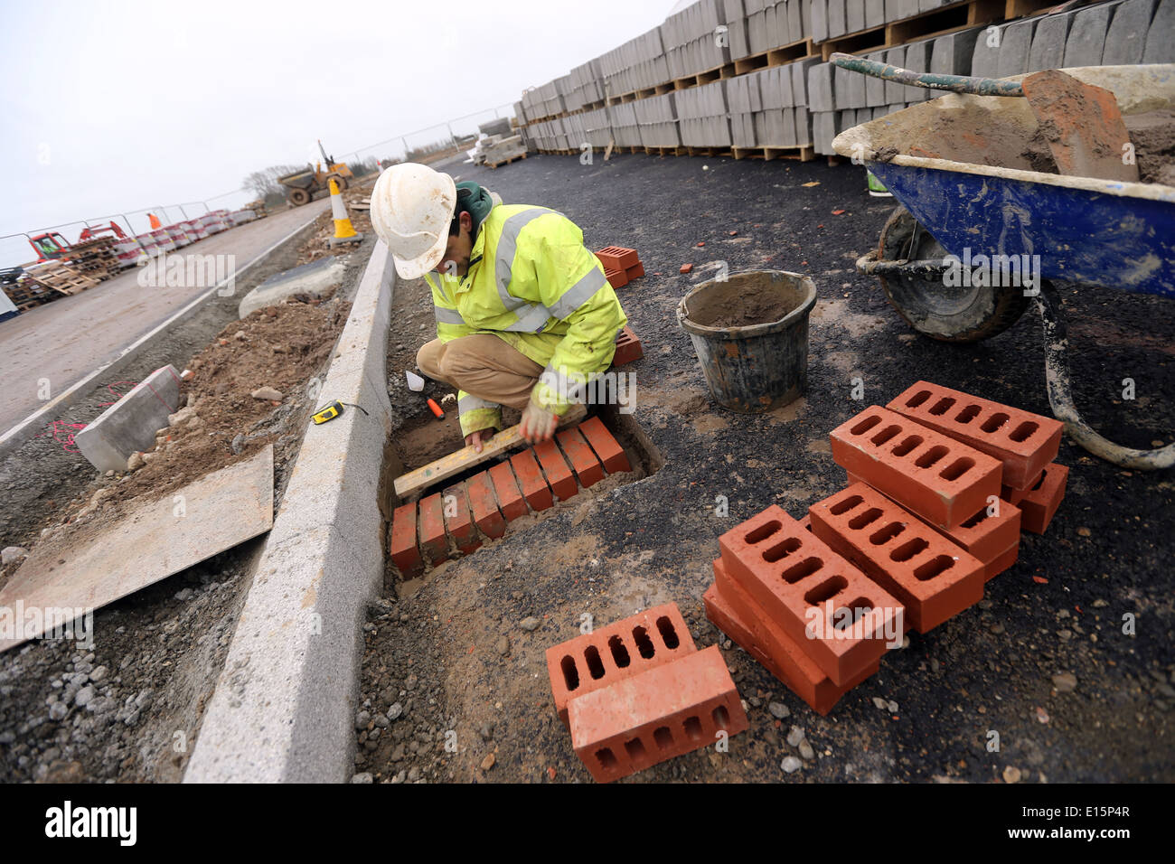 Tradesman workman on a building site brick laying around a drainage section on a road. Stock Photo