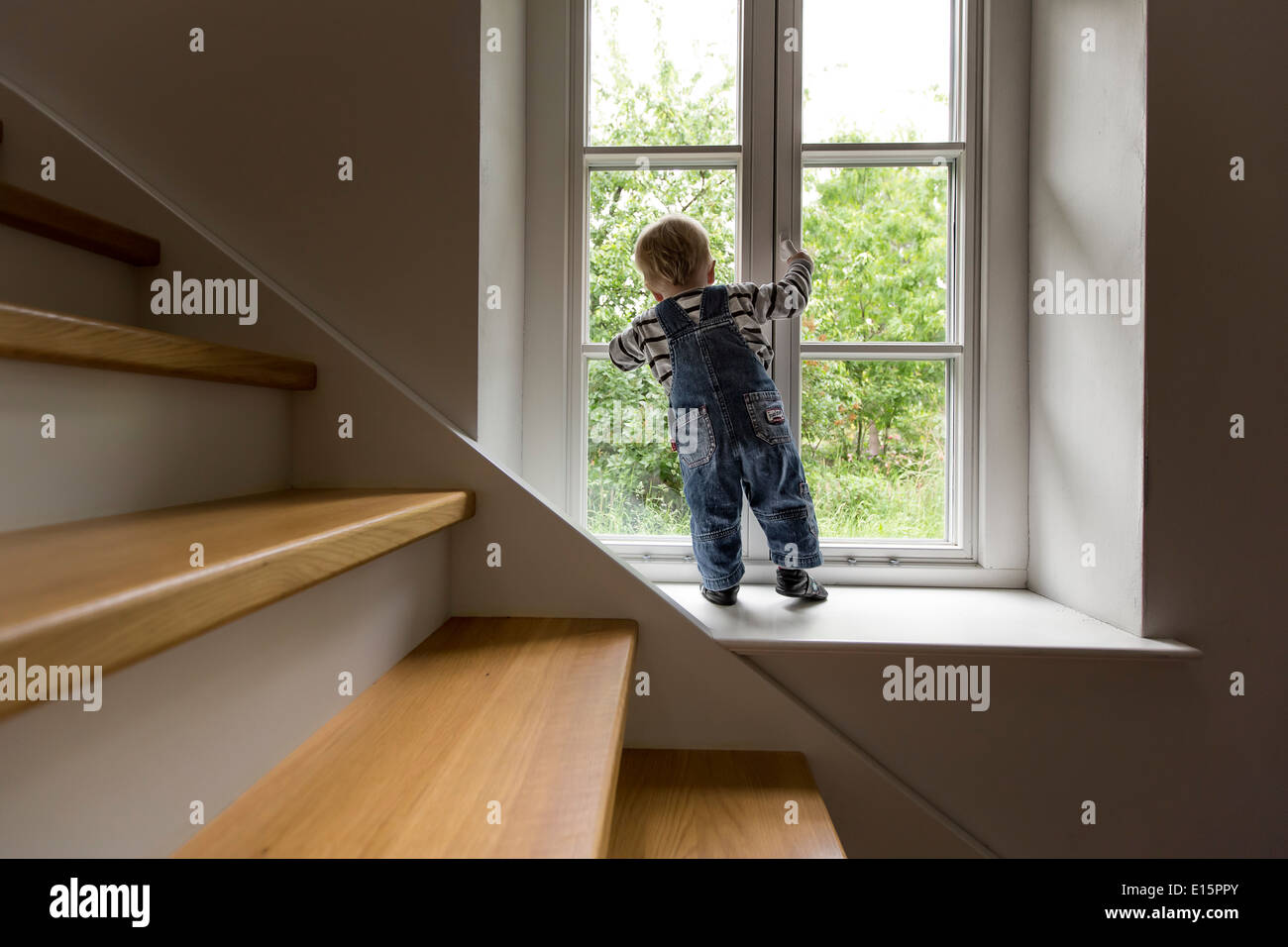 Infant, boy 1 year, looking out of the window into the garden, holding the window handle. Stock Photo