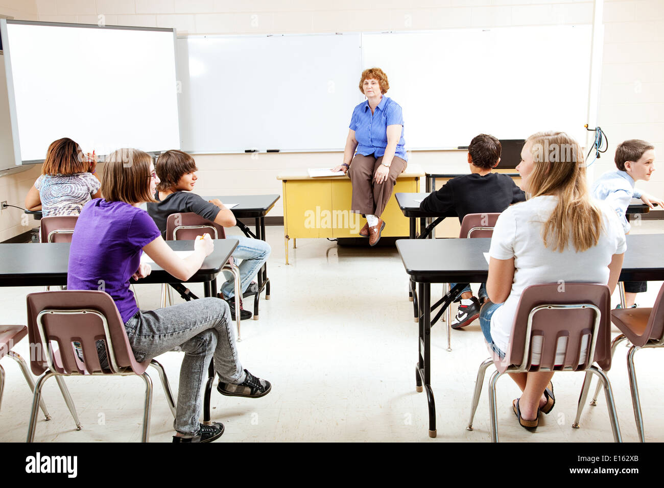 Teacher sitting on her desk, teaching a class of teenage students Stock