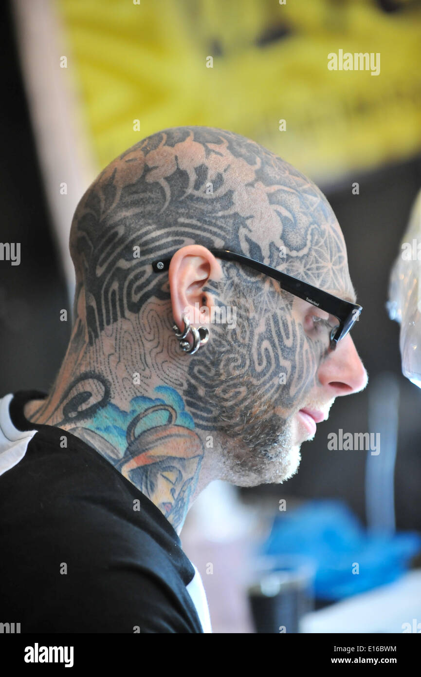 Alexandra Palace, London, UK. 24th May 2014. A tattooist with his face covered in tattoos concentrates on his work at the Great British Tattoo Show taking place this weekend at Alexandra Palace. The show features tattooing,  stall selling clothing and accessories, wrestling and a fashion show Credit:  Matthew Chattle/Alamy Live News Stock Photo