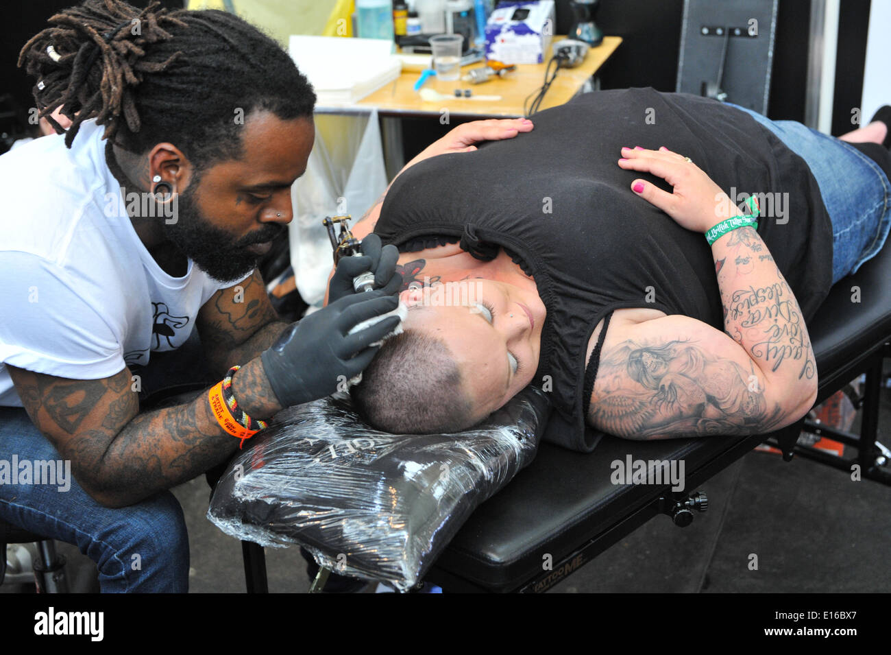 Alexandra Palace, London, UK. 24th May 2014. A tattoo artist at work on a womans head at the Great British Tattoo Show taking place this weekend at Alexandra Palace. The show features tattooing,  stall selling clothing and accessories, wrestling and a fashion show Credit:  Matthew Chattle/Alamy Live News Stock Photo