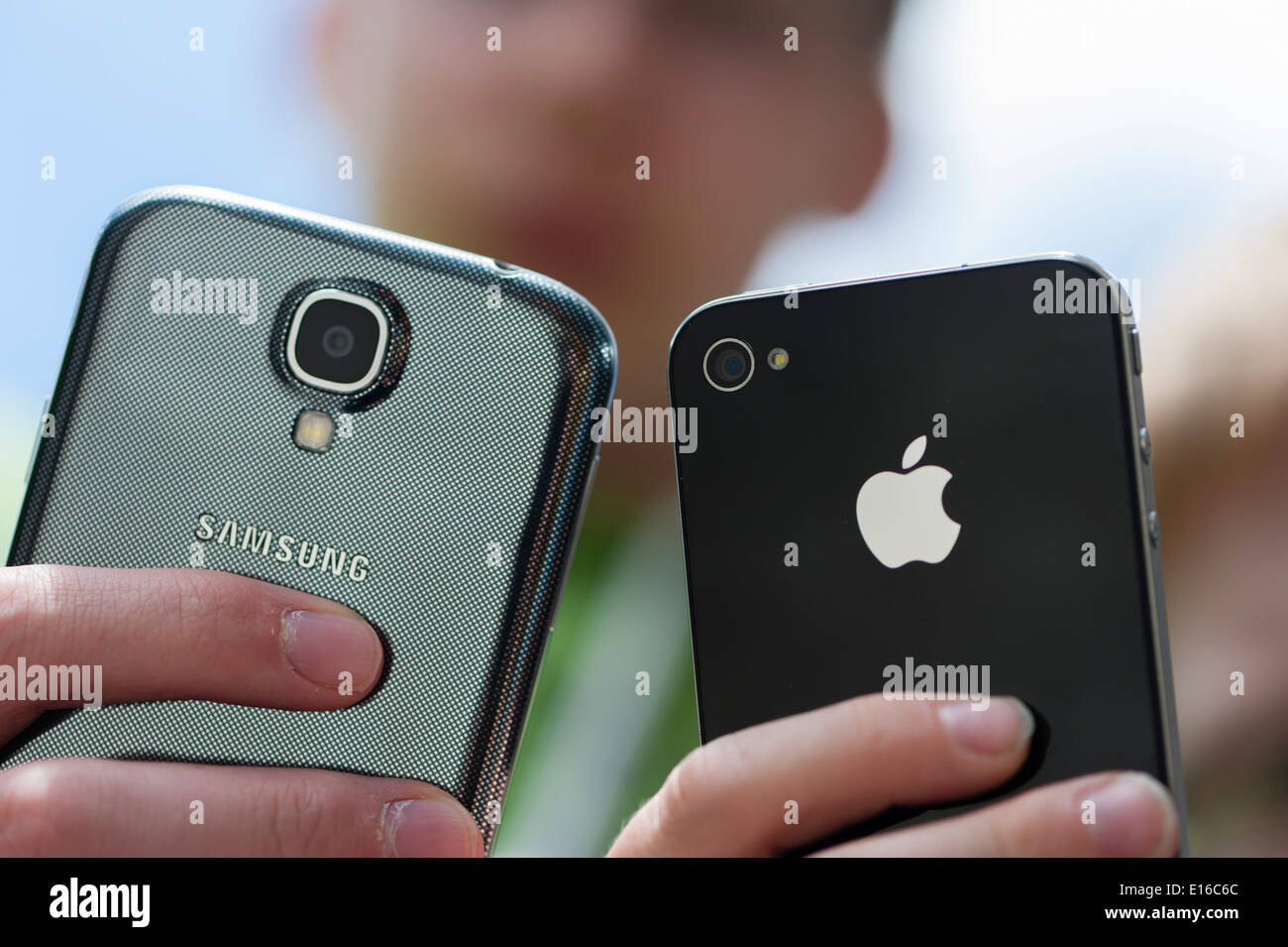 Two teenagers are posing with their Samsung Galaxy S4 (left) and iPhone 4 smartphones. Stock Photo