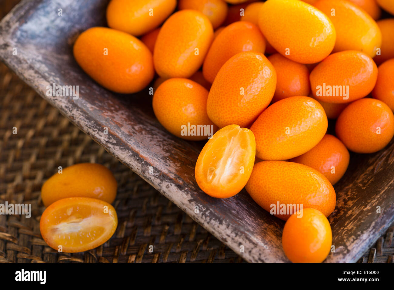 Kumquats in square ceramic bowl on woven rustic tray Stock Photo