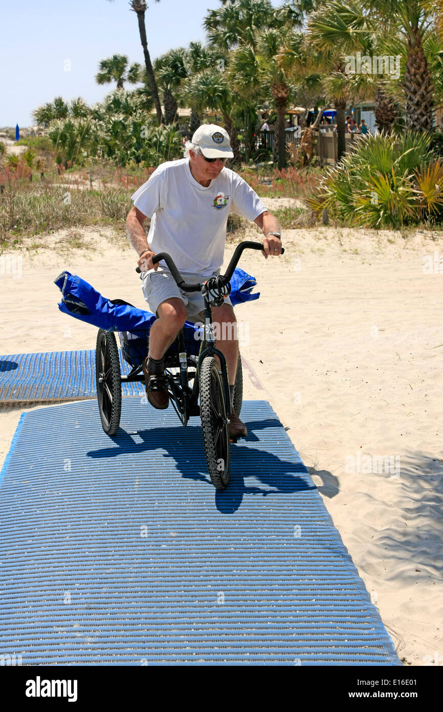 Senior male riding a tricycle on a beach mat pathway Stock Photo