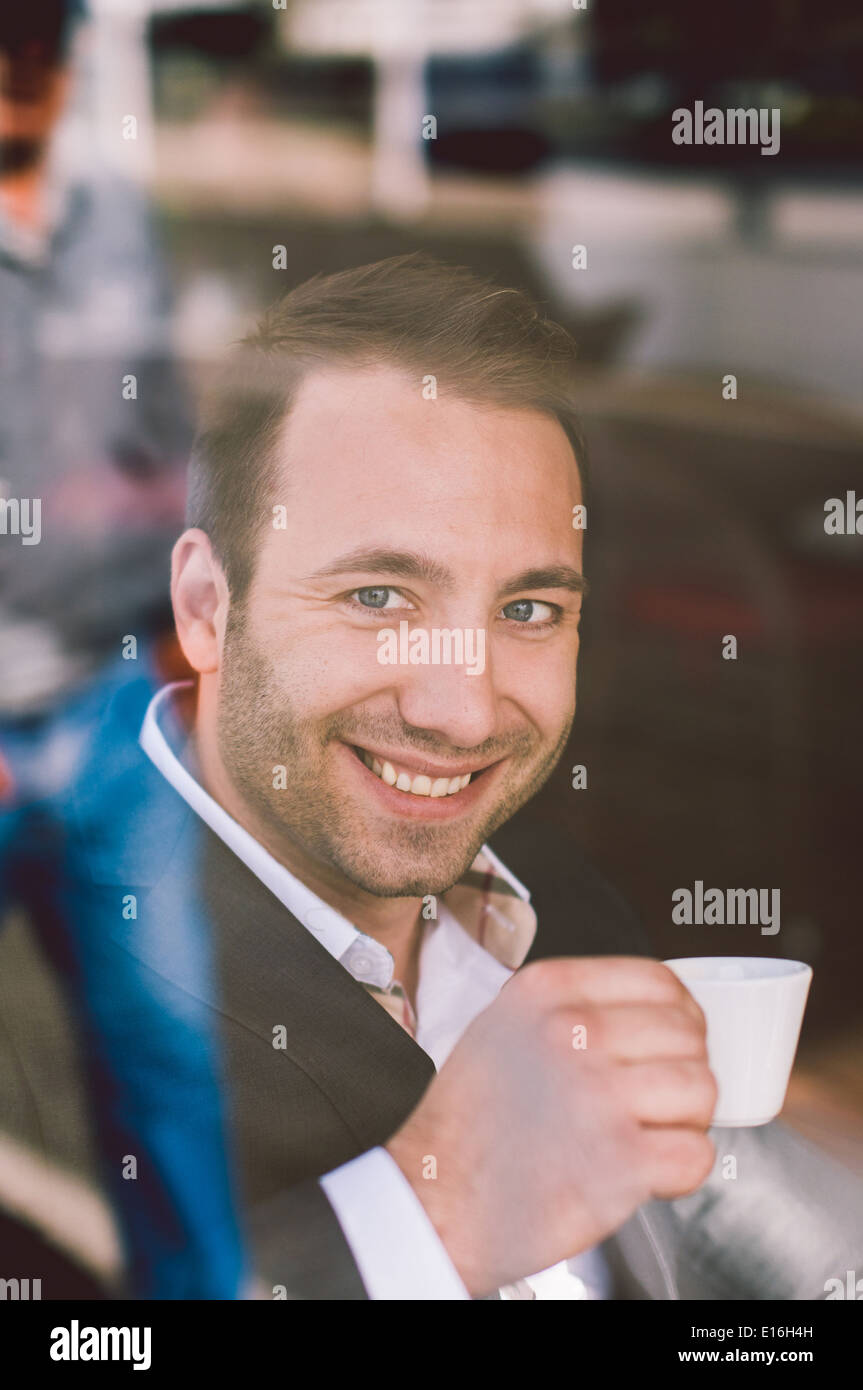 Handsome smiling man drinking espresso in cafe looking through the window Stock Photo