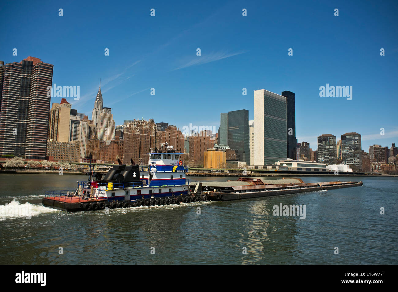 Tugboat pushing barges of gravel on New York City's East River, Chrysler Building and United Nations building in background Stock Photo