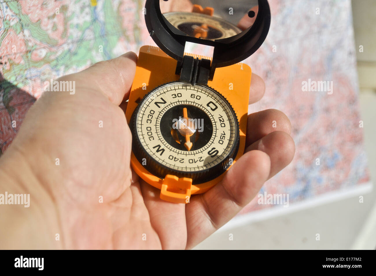 Open compass mirror cover in the palm of a man lying on the background of topographic maps. Stock Photo