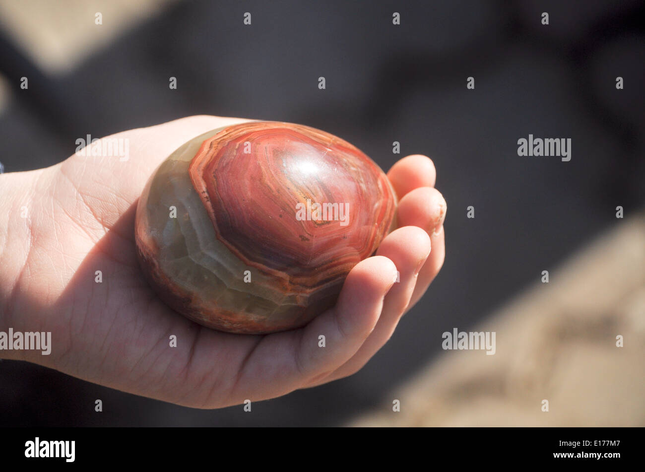 Easter egg made of Jasper lies in the hand and lit by the rays of the sun. Stock Photo