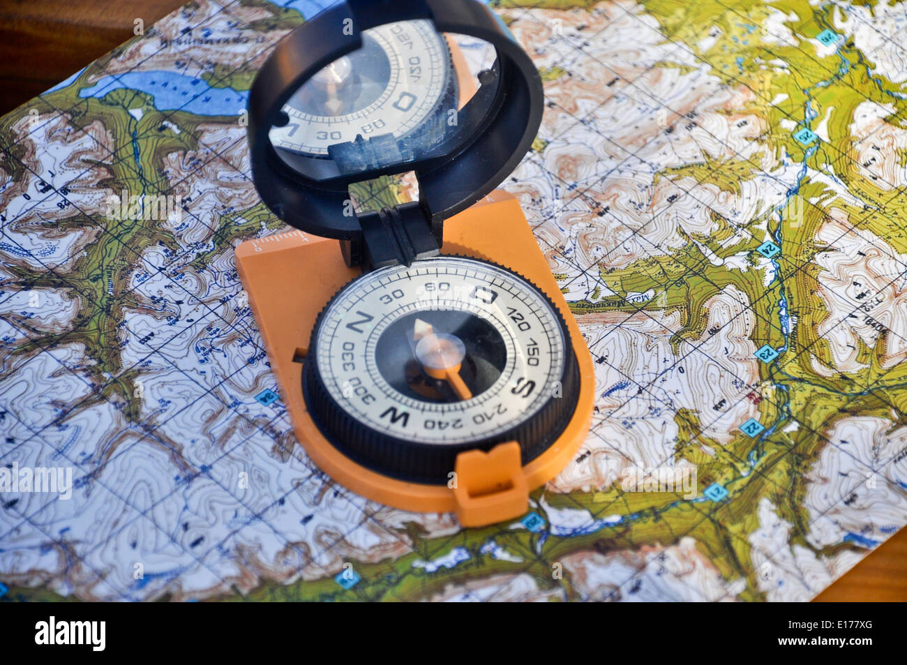 Orange compass mirror cover lies on topographic maps. Compass on the map Stock Photo
