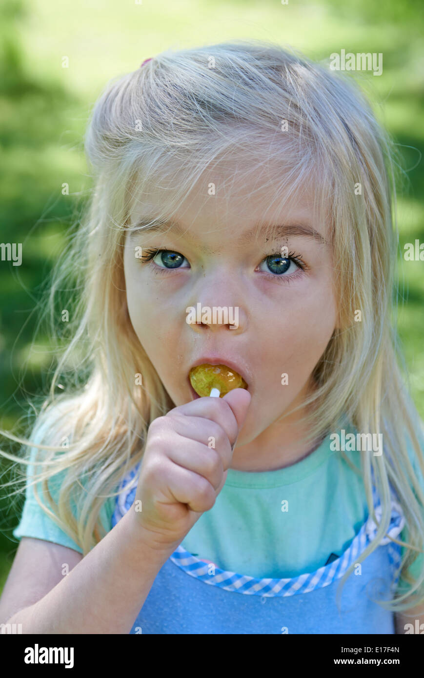 Little child blond girl licking lollipop outside in garden, portrait Stock Photo