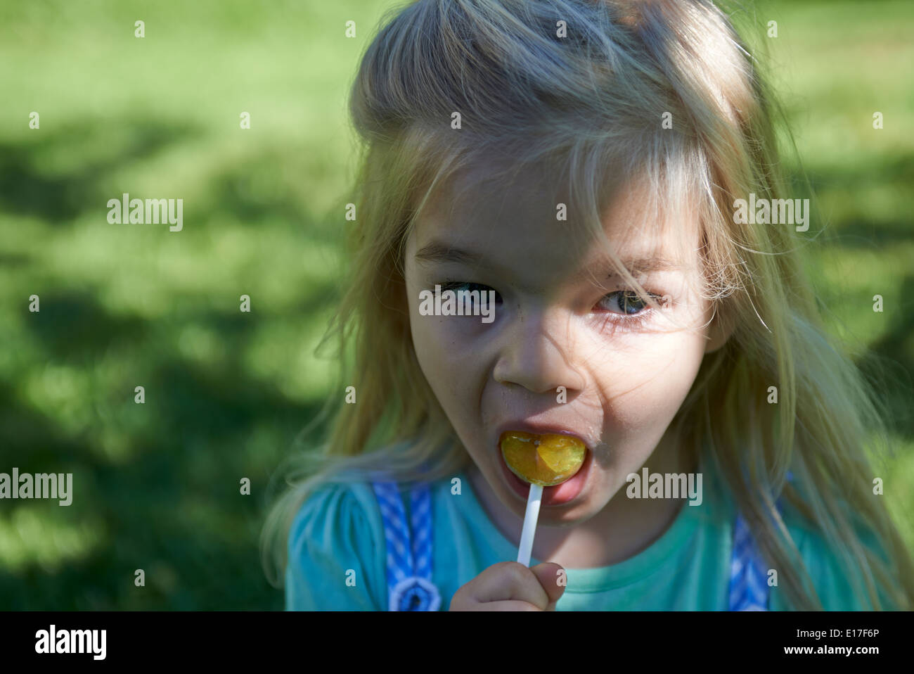 Little child blond girl licking lollipop outside in garden, portrait Stock Photo